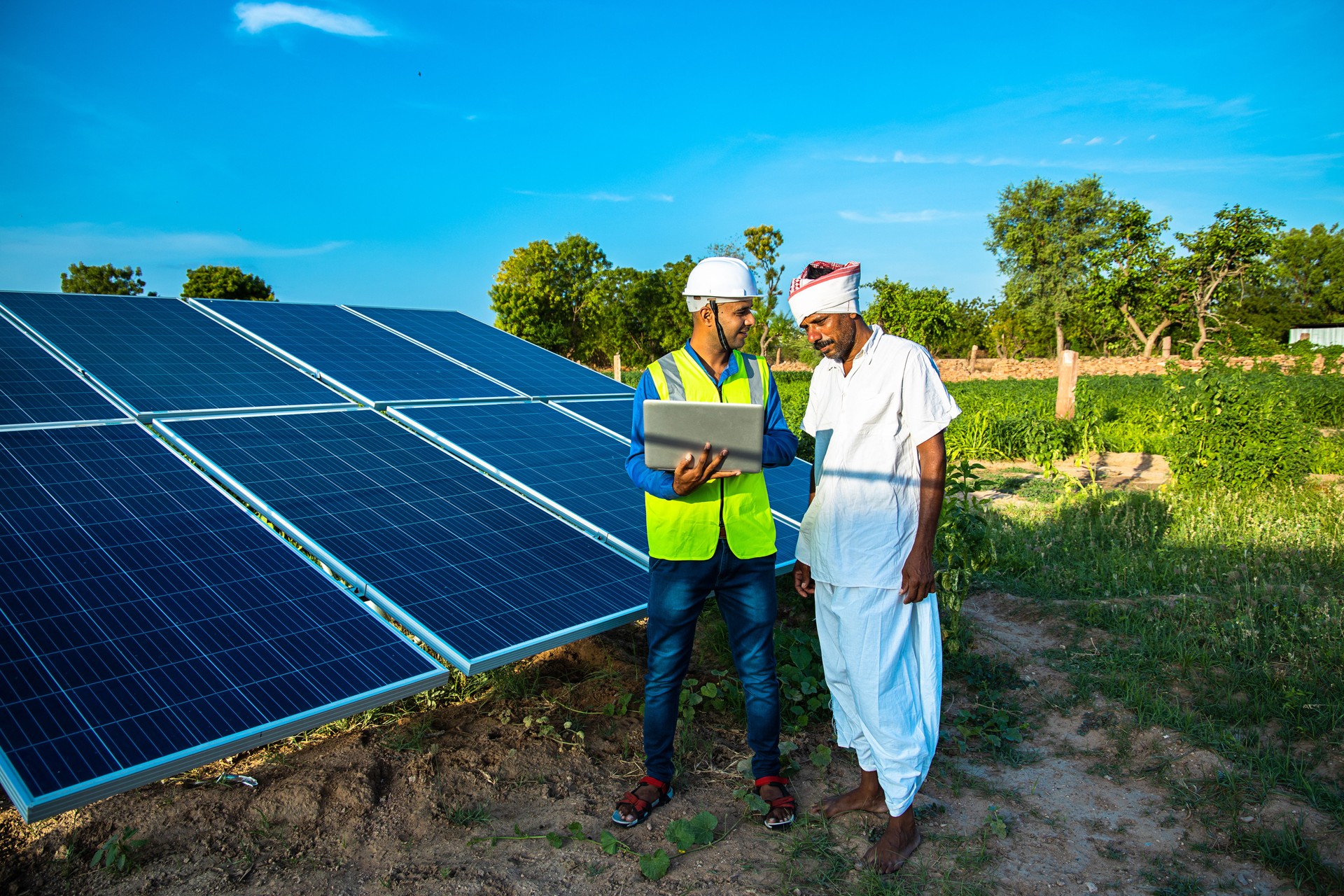 young male technician worker wearing green vests and helmet checks the maintenance of the solar panels and talking about installation of new solar panel with farmer at field, technology in agriculture young male technician worker wearing green vests and helmet checks the maintenance of the solar panels and talking about installation of new solar panel with farmer at field, technology in agriculture